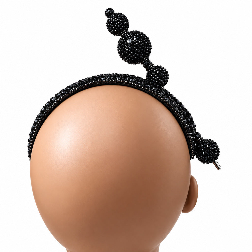 A black beaded headband with three large round beads and smaller accent beads, displayed on a mannequin head against a white wall.