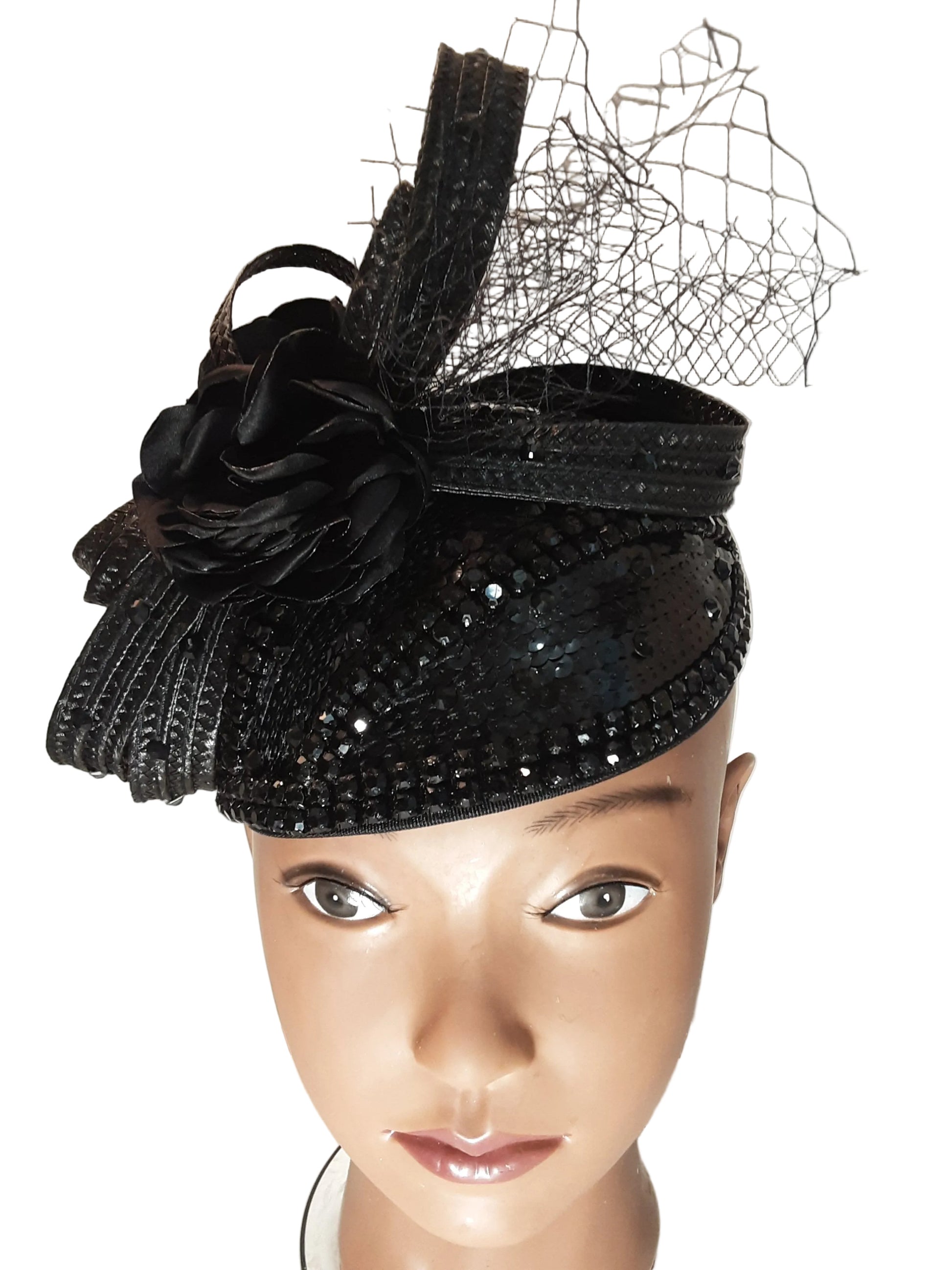 A black embellished fascinator hat with a large fabric flower and sheer netting, displayed on a mannequin head against a plain light background.