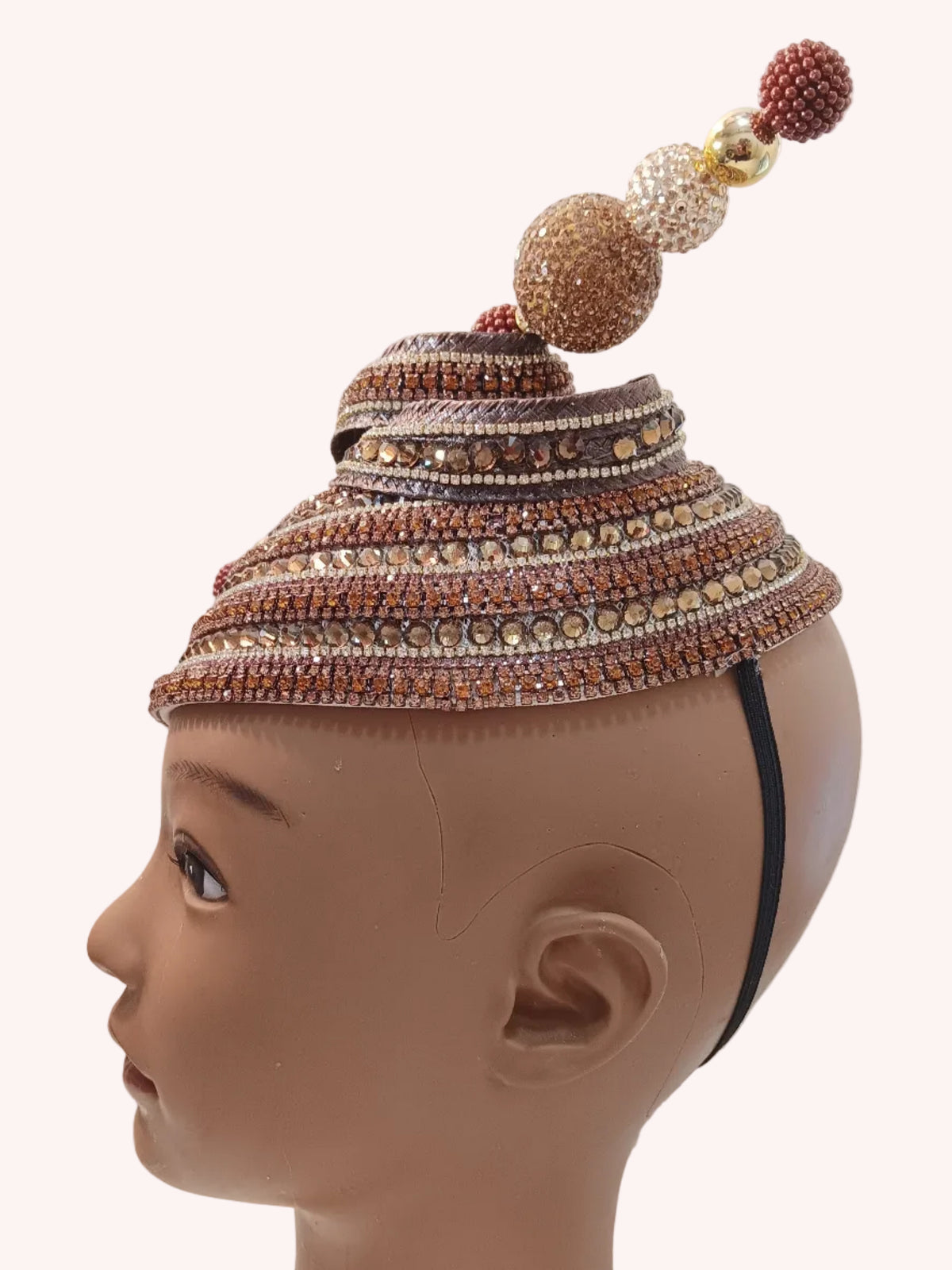 A beaded traditional cap with a tall decorative top, displayed on a mannequin head against a white wall.