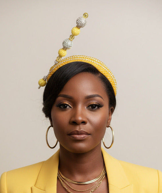 A yellow beaded headband with a tall decorative spike featuring yellow and silver rhinestone beads, displayed on a mannequin head against a white wall.