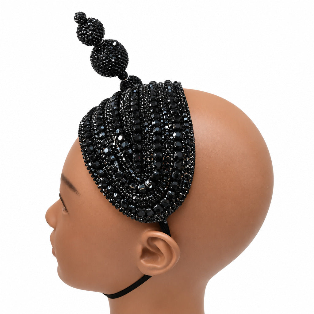 A black beaded headpiece with a tall central puff and three dangling bead clusters, displayed on a mannequin head against a plain white wall.