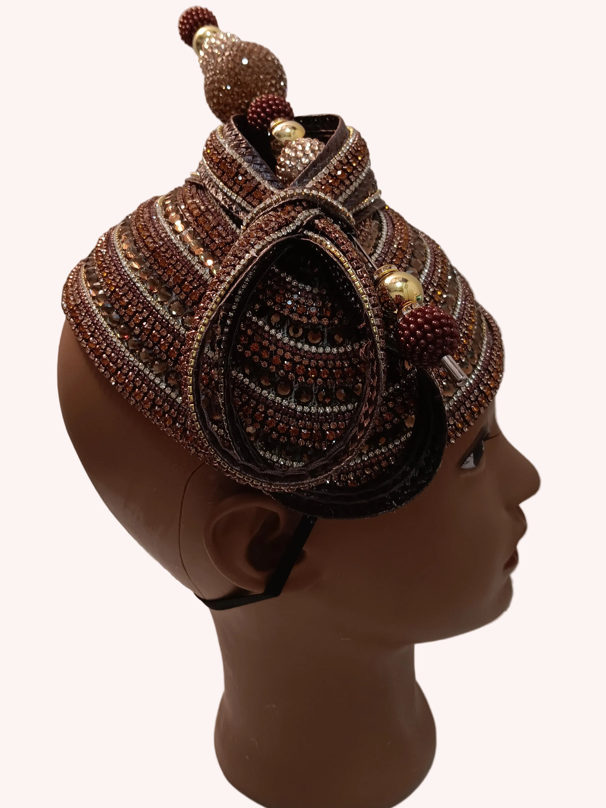 An ornate traditional African beaded hat displayed on a mannequin head against a textured off-white wall.