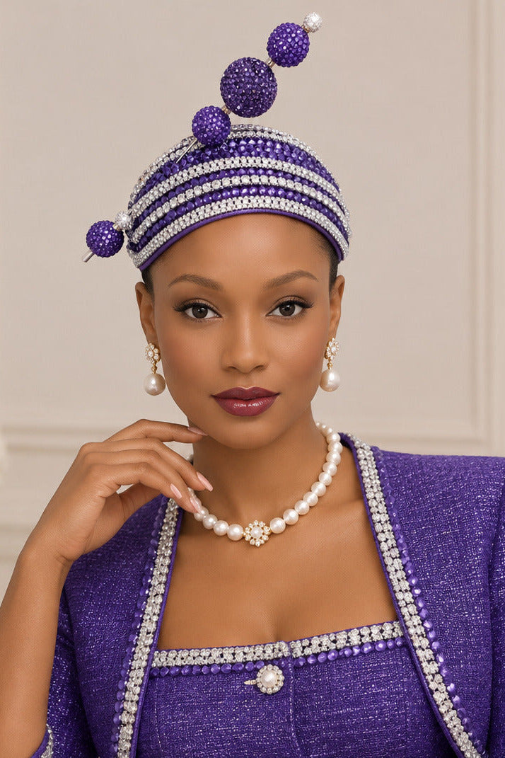 A purple and silver rhinestone embellished headband with three large purple rhinestone pom-poms and two smaller side pom-poms, displayed on a mannequin head against a white wall.