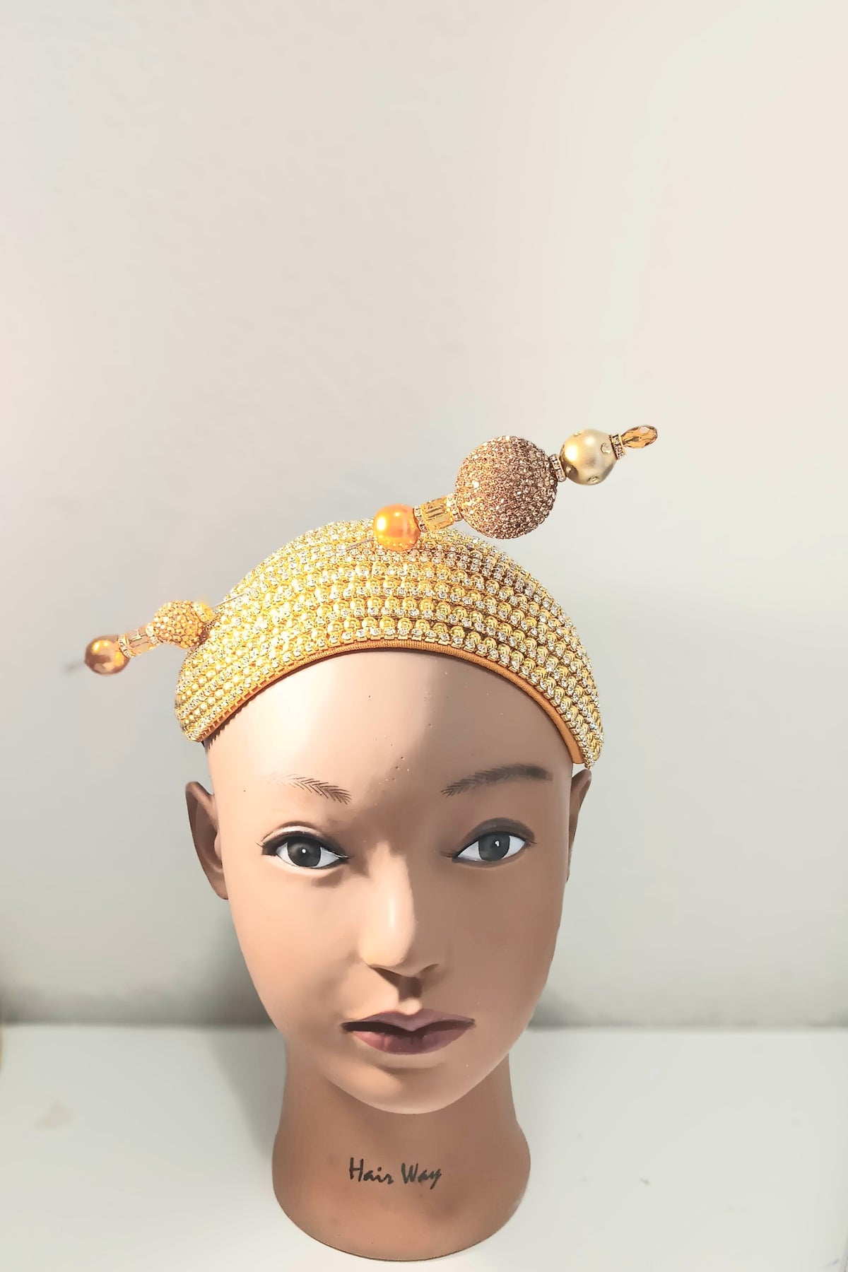 A gold beaded headpiece with decorative beads and tassels displayed on a mannequin head against a plain light background.